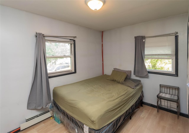 bedroom with light hardwood / wood-style floors, a baseboard heating unit, and multiple windows