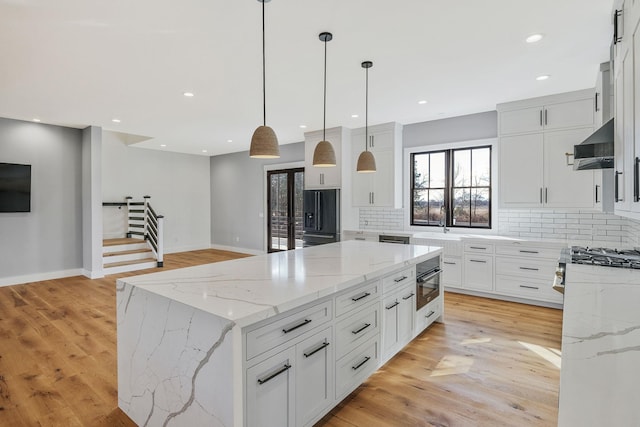 kitchen with pendant lighting, a center island, light hardwood / wood-style floors, light stone counters, and white cabinetry