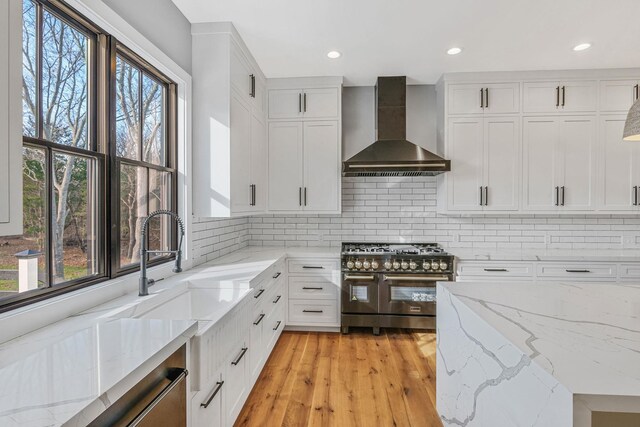 kitchen with range with two ovens, a healthy amount of sunlight, and wall chimney range hood