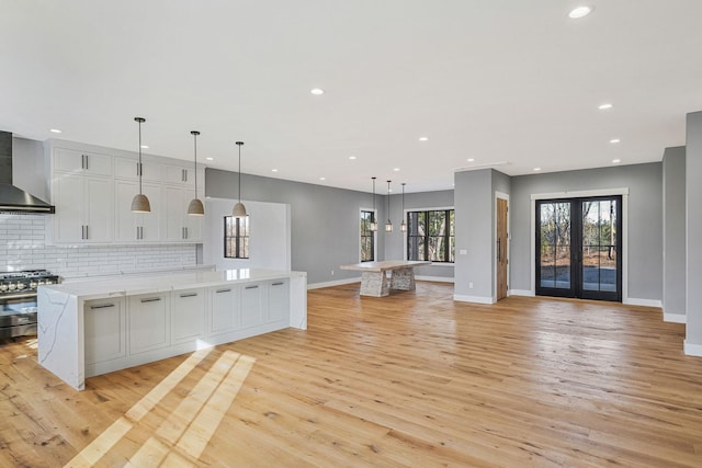 kitchen with high end range, a spacious island, wall chimney range hood, pendant lighting, and light hardwood / wood-style flooring