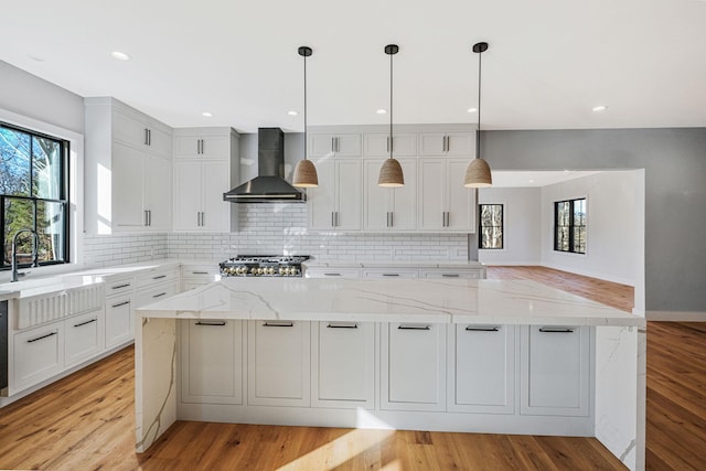 kitchen with white cabinets, light stone countertops, light hardwood / wood-style flooring, and wall chimney exhaust hood