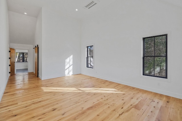 unfurnished living room with light wood-type flooring, a barn door, and high vaulted ceiling