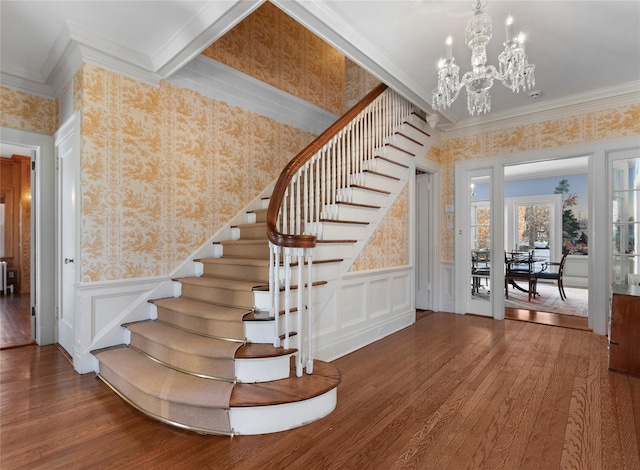 stairs featuring wood-type flooring, ornamental molding, and an inviting chandelier