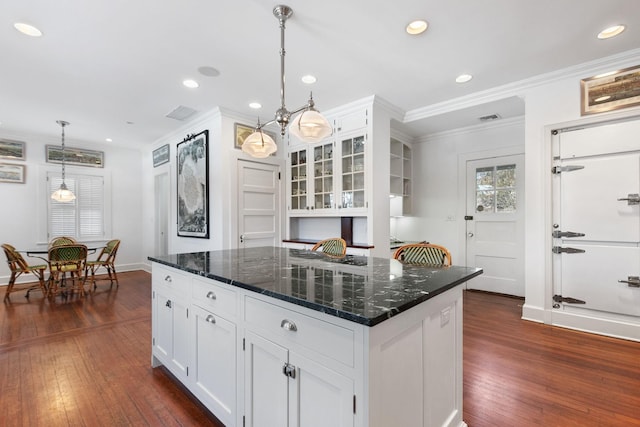 kitchen featuring dark wood-type flooring, dark stone counters, a kitchen island, pendant lighting, and white cabinets