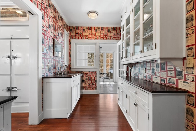 bar with dark wood-type flooring, sink, white cabinets, and ornamental molding