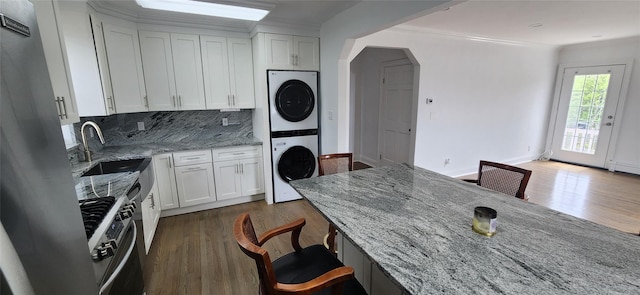 kitchen with white cabinetry, light stone counters, stacked washer / dryer, and sink