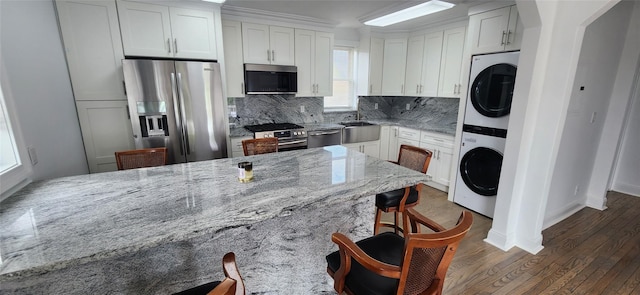 kitchen with light stone countertops, appliances with stainless steel finishes, white cabinetry, and stacked washer / drying machine