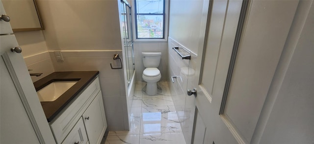 bathroom featuring vanity, toilet, a shower with door, and tile walls