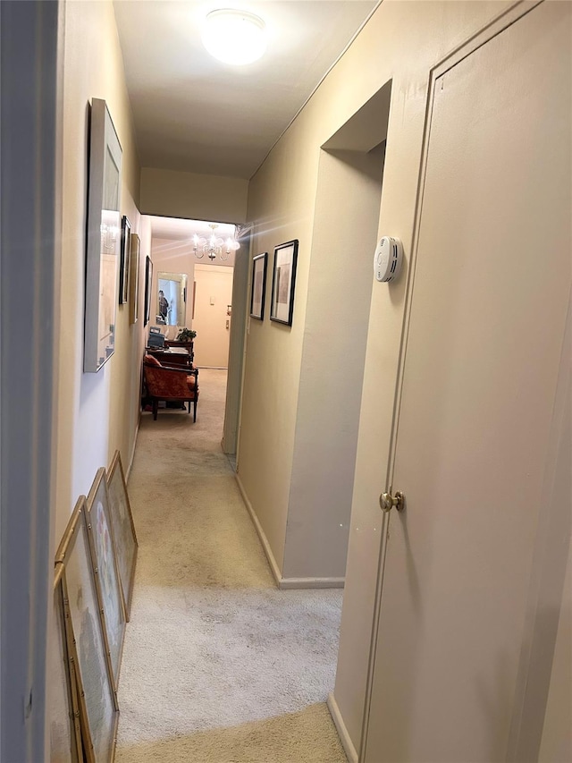 hallway with light colored carpet and an inviting chandelier