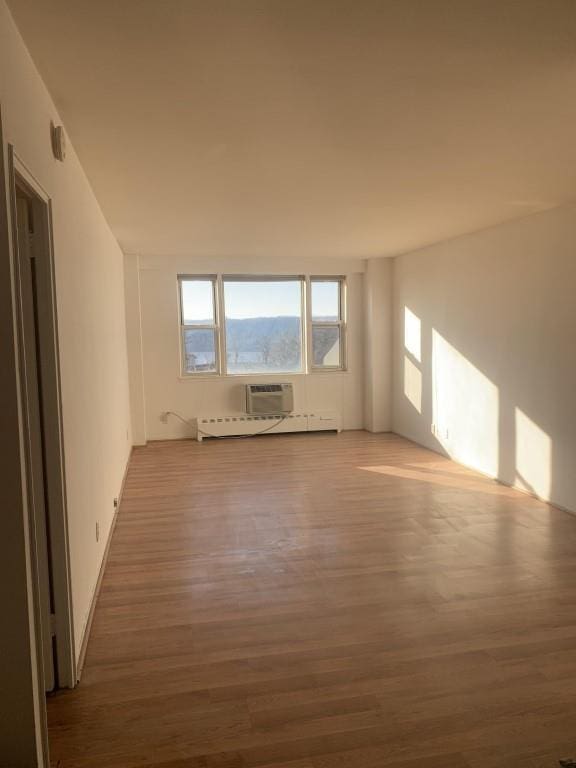 spare room featuring hardwood / wood-style flooring, an AC wall unit, and a baseboard heating unit