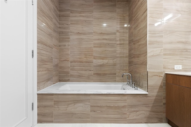 bathroom featuring tile walls, tiled bath, and vanity