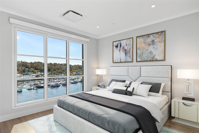 bedroom featuring light hardwood / wood-style floors, crown molding, a water view, and multiple windows