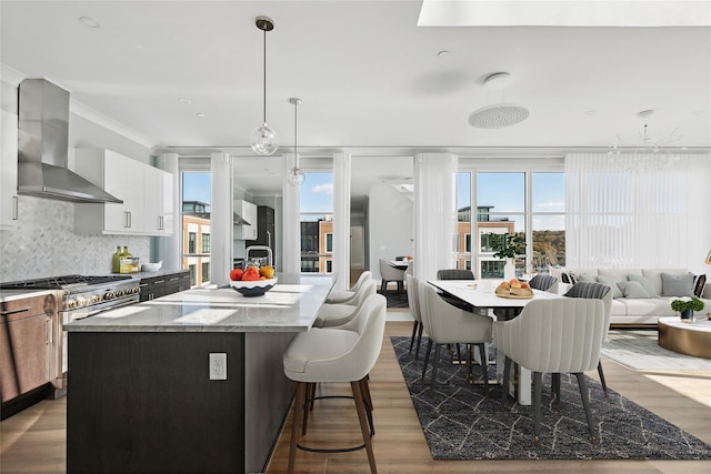 kitchen with gas range, pendant lighting, a center island with sink, wall chimney range hood, and tasteful backsplash