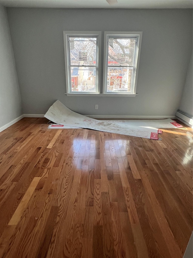 unfurnished room with hardwood / wood-style floors and a baseboard heating unit