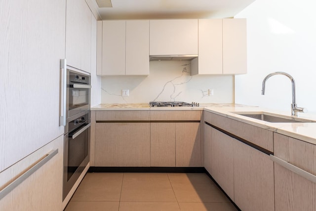 kitchen featuring stainless steel gas stovetop, light tile patterned floors, sink, and light brown cabinetry