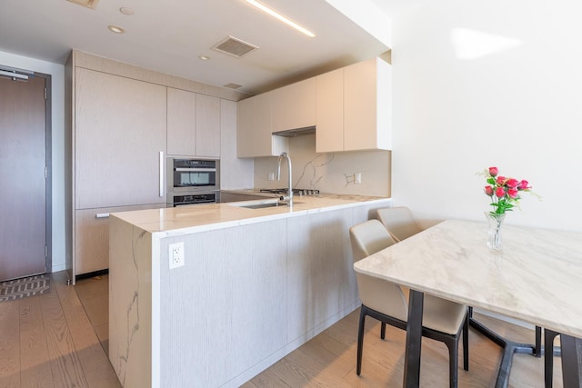 kitchen with kitchen peninsula, stainless steel oven, and light hardwood / wood-style flooring