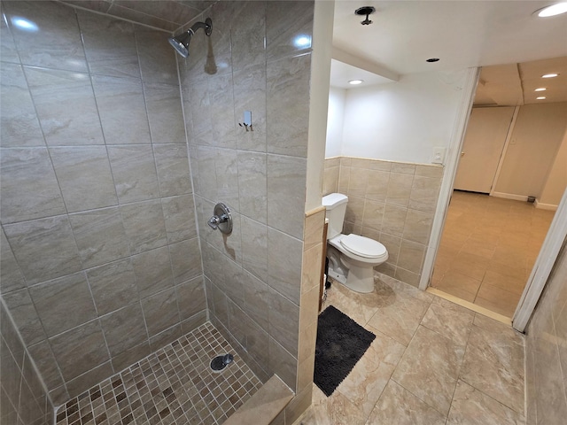 bathroom with tile patterned floors, toilet, tile walls, and tiled shower