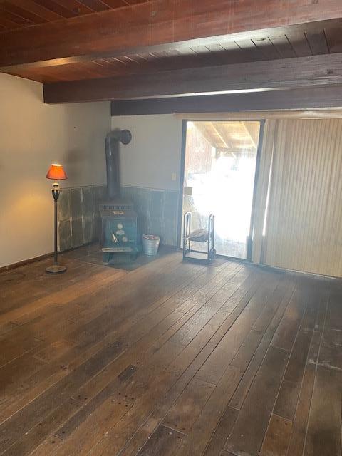 unfurnished living room with beam ceiling, a wood stove, dark wood-type flooring, and wooden ceiling