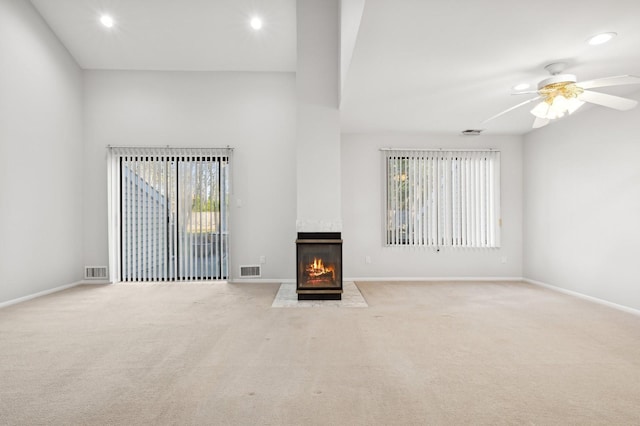 unfurnished living room with light carpet, a large fireplace, and ceiling fan