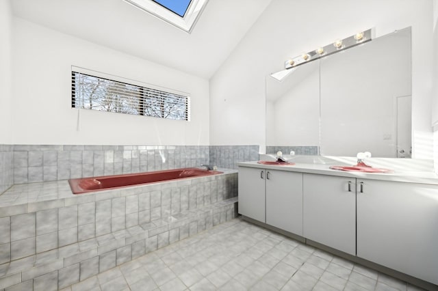 bathroom featuring vanity, tiled bath, and lofted ceiling with skylight