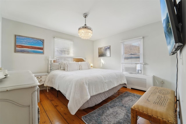 bedroom featuring hardwood / wood-style flooring, radiator heating unit, cooling unit, and a notable chandelier