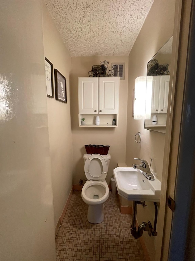 bathroom with a textured ceiling, toilet, and sink