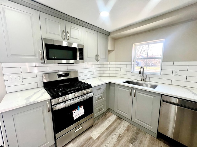 kitchen featuring gray cabinets, appliances with stainless steel finishes, tasteful backsplash, sink, and light hardwood / wood-style flooring