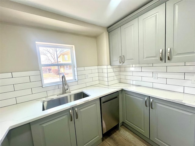 kitchen with light stone counters, stainless steel dishwasher, sink, and decorative backsplash