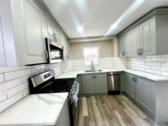 kitchen featuring sink, gray cabinetry, stainless steel appliances, light hardwood / wood-style floors, and decorative backsplash