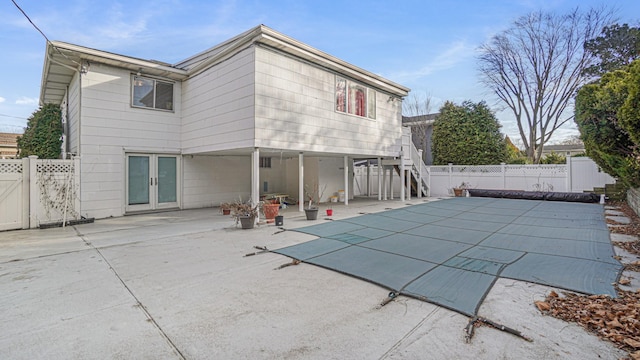 rear view of property featuring a covered pool, a patio area, and french doors