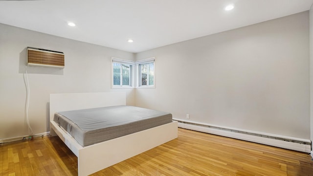 bedroom with baseboard heating, wood-type flooring, and a wall mounted air conditioner