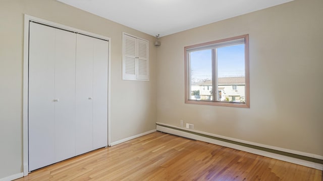 unfurnished bedroom featuring light hardwood / wood-style floors, a closet, and a baseboard heating unit