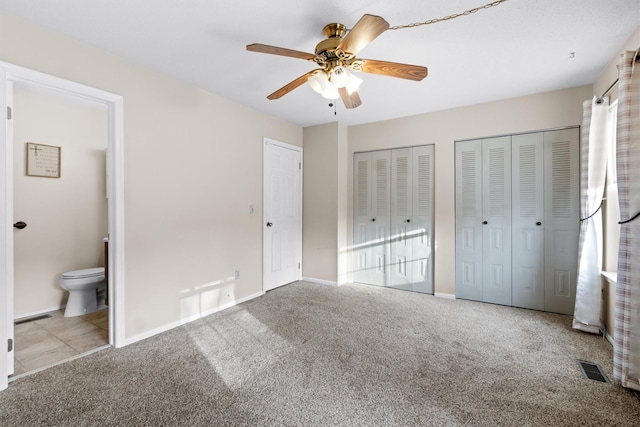 unfurnished bedroom featuring ensuite bathroom, ceiling fan, light colored carpet, and multiple closets