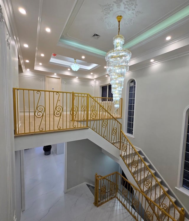 stairs featuring a raised ceiling, ornamental molding, and a notable chandelier