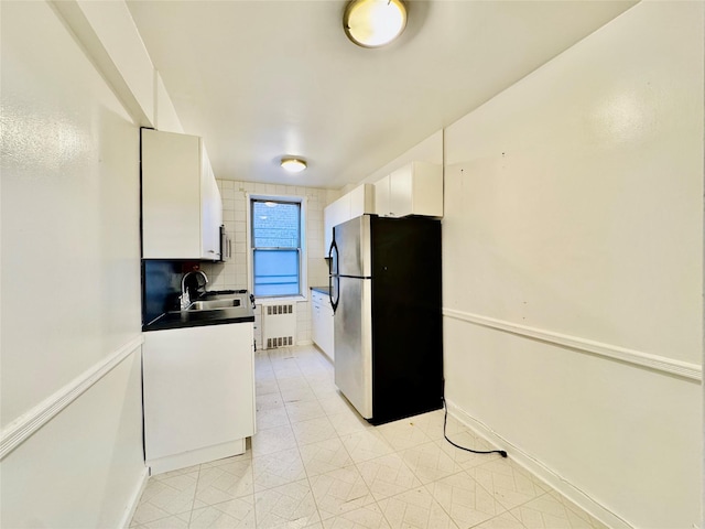 kitchen with stainless steel fridge, tasteful backsplash, sink, radiator heating unit, and white cabinetry