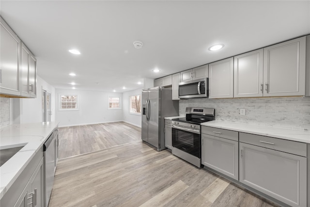 kitchen with gray cabinets, light stone countertops, stainless steel appliances, and light wood-type flooring