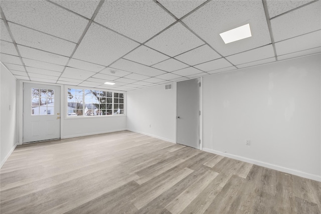 basement with light wood-type flooring and a paneled ceiling