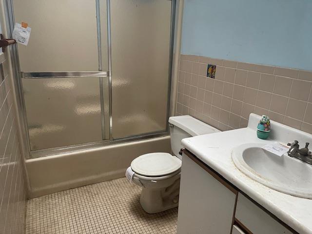 full bathroom featuring tile patterned flooring, combined bath / shower with glass door, toilet, vanity, and tile walls