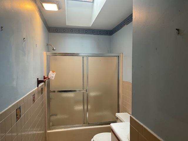 full bathroom featuring vanity, toilet, enclosed tub / shower combo, and tile walls