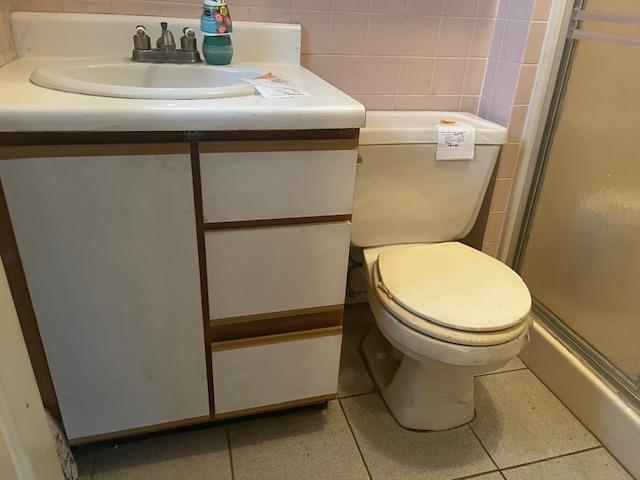 bathroom featuring a shower with door, vanity, tile walls, and toilet