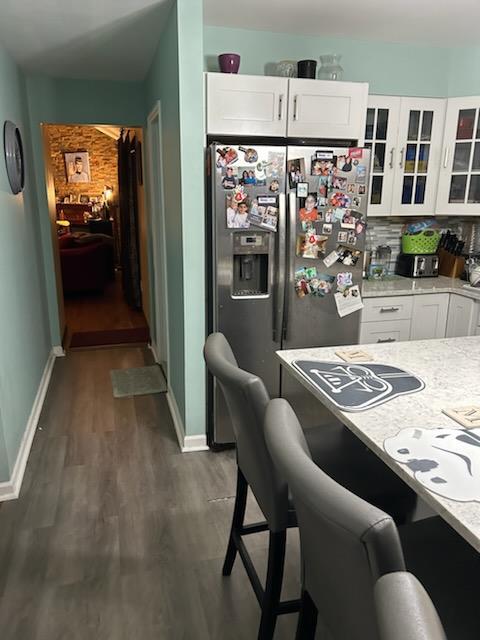 kitchen with white cabinetry, light stone countertops, dark hardwood / wood-style flooring, backsplash, and stainless steel fridge