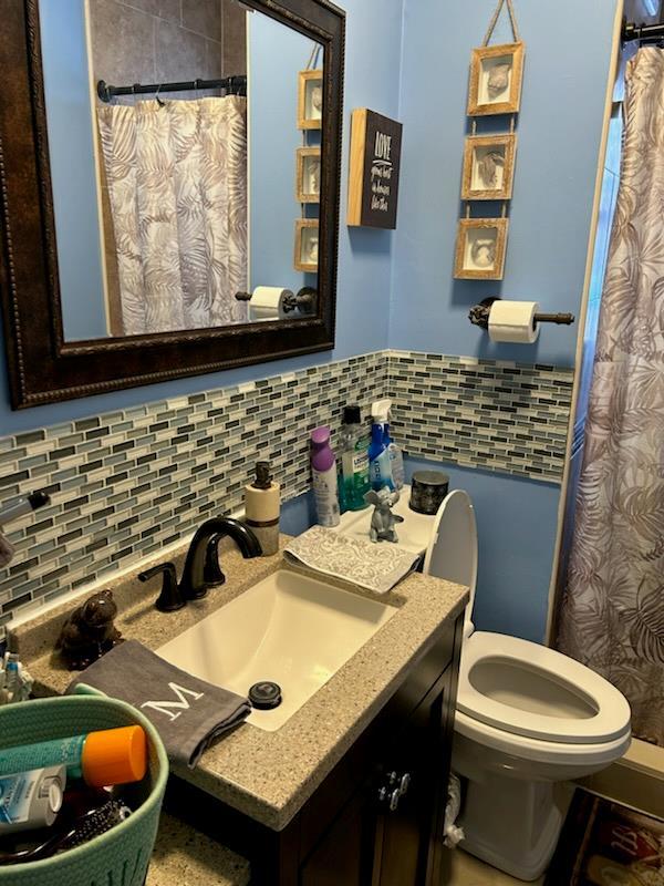 bathroom with a shower with shower curtain, vanity, toilet, and backsplash