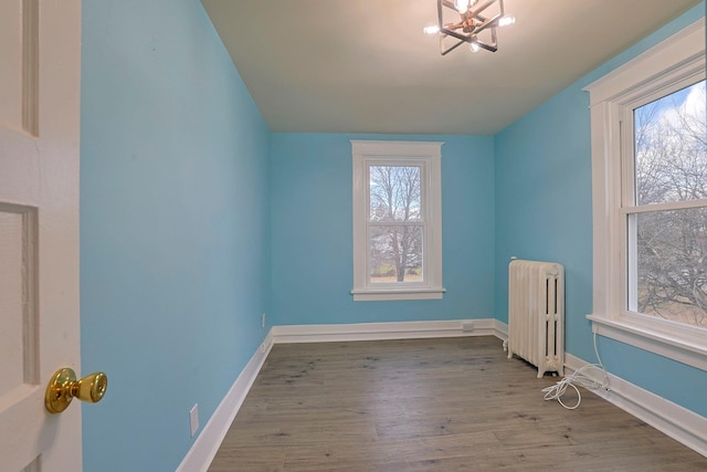 empty room with hardwood / wood-style flooring, radiator heating unit, and a chandelier