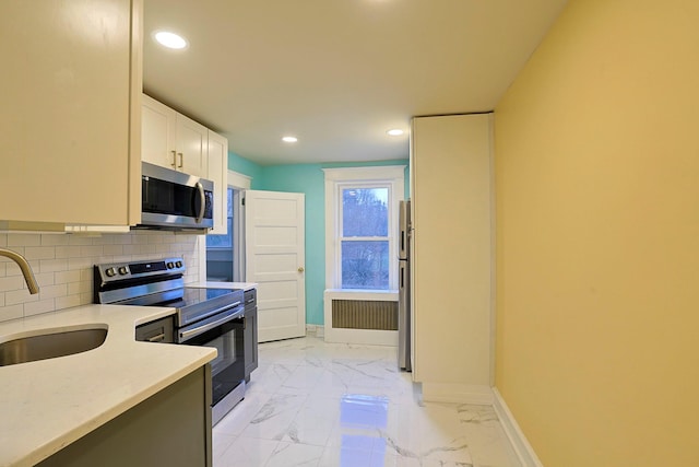 kitchen featuring radiator heating unit, sink, decorative backsplash, white cabinets, and appliances with stainless steel finishes