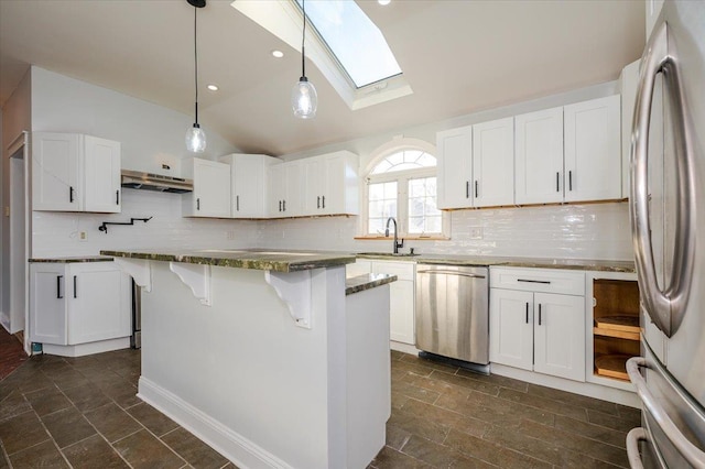 kitchen with vaulted ceiling with skylight, white cabinets, stainless steel appliances, and a kitchen island