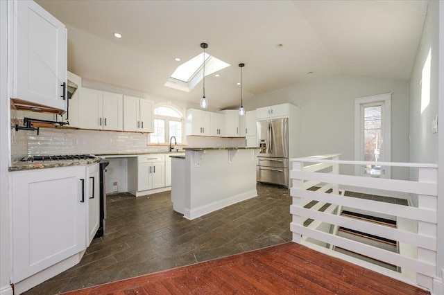 kitchen featuring a center island, dark wood-type flooring, white cabinets, vaulted ceiling with skylight, and stainless steel appliances