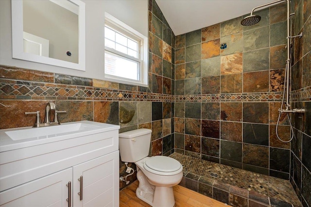 bathroom featuring a tile shower, vanity, wood-type flooring, tile walls, and toilet