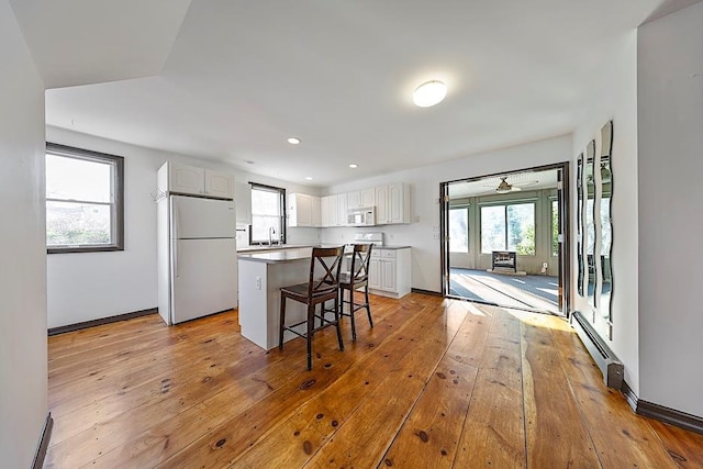 kitchen featuring white appliances, a kitchen breakfast bar, light wood-type flooring, a center island, and white cabinetry