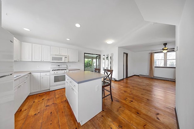 kitchen featuring white appliances, a breakfast bar area, light wood-type flooring, a kitchen island, and white cabinets