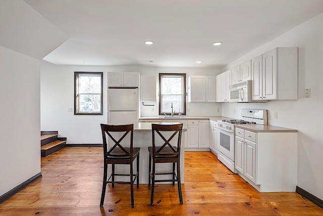 kitchen featuring sink, white cabinetry, a center island, white appliances, and a breakfast bar